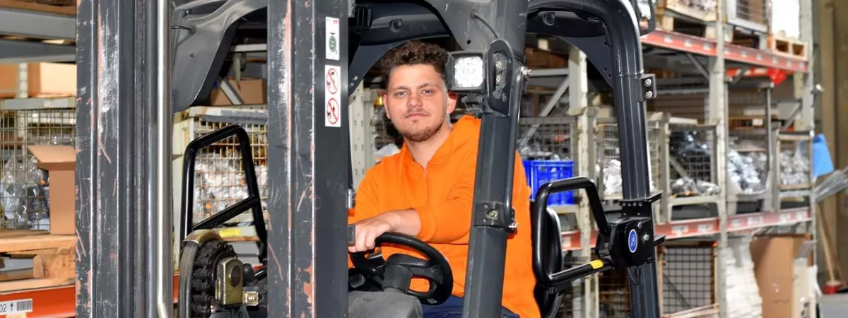 Junger Auszubildender in orangener Jacke sitzt auf einem Gabelstapler