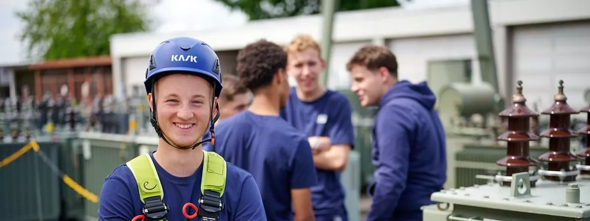 Junger Auszubildender steht mit Klettergurt vor Trafos