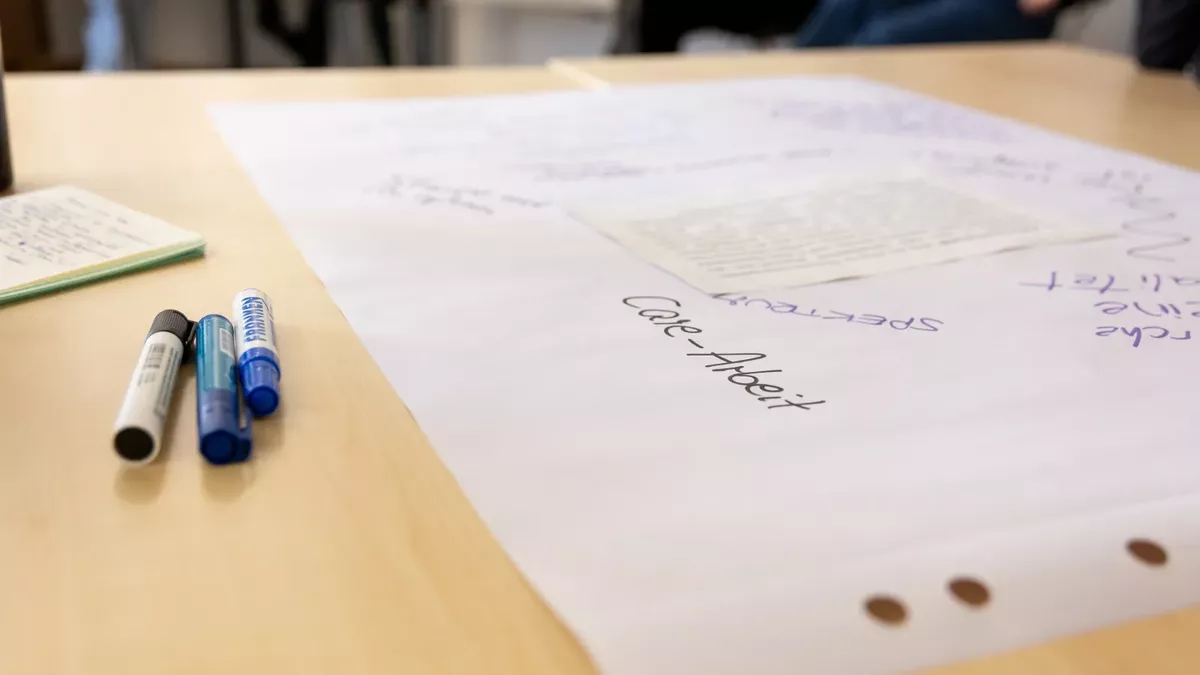 Auf einem Tisch liegen Stifte und ein Blatt Papier, auf dem das Wort 