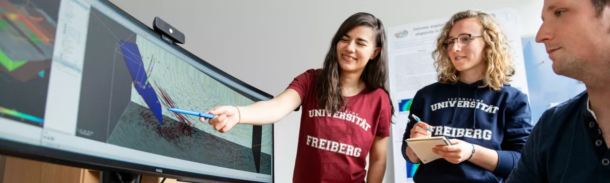 Zwei Studentinnen zeigen einem Dozenten etwas auf dem Bildschirm