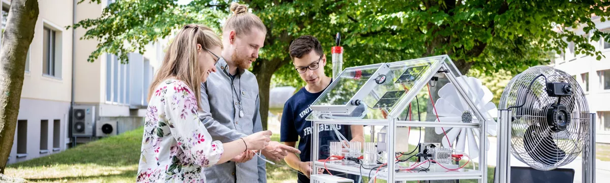 Drei Studierende betrachten ein Modell eines energieautarken Hauses