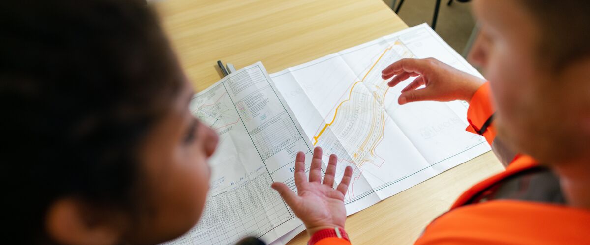 Ingenieurin und Ingenieur stehen über einen Plan gebeugt